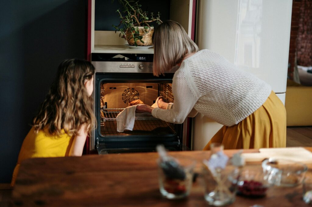 A mother and daughter in front of an oven baking a loaf of bread