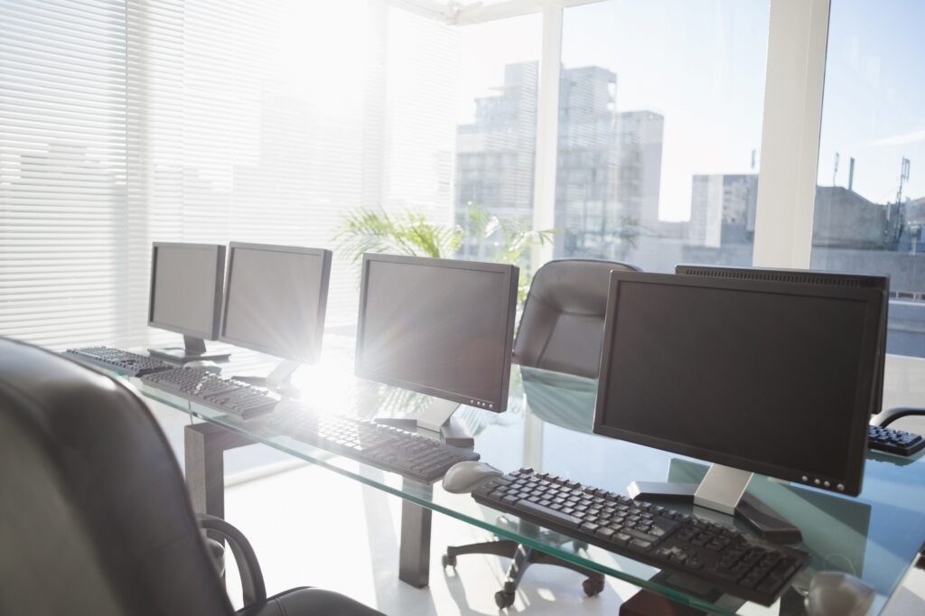 A row of computers on a glass table in the office