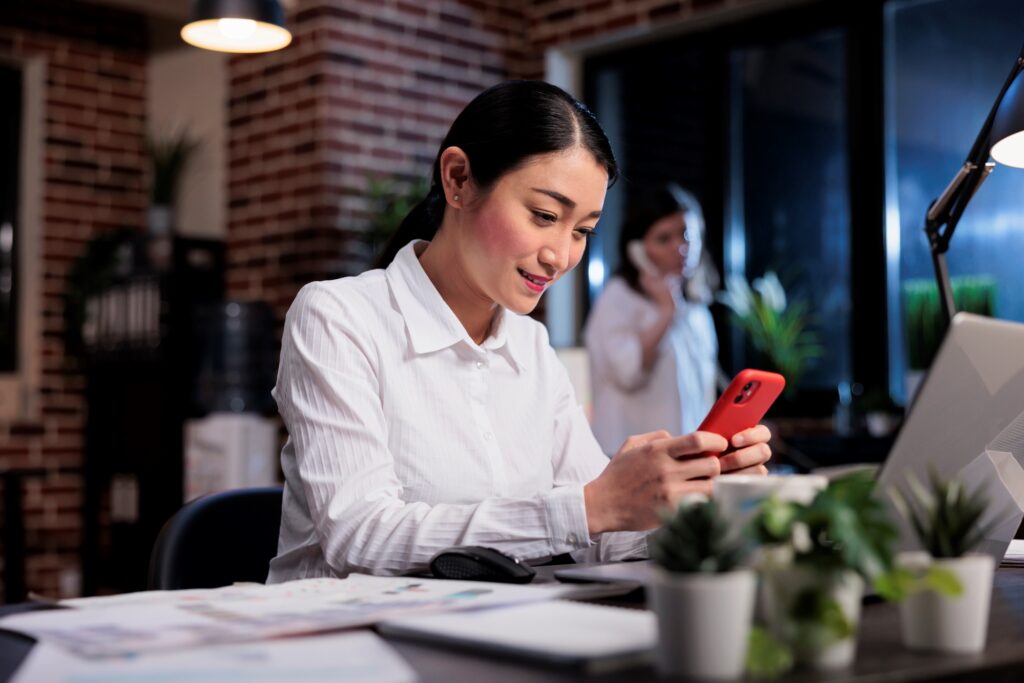 A smiling female employee sending an office relocation message via mobile phone